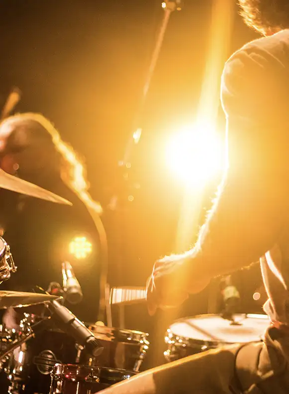 Bild von 2 Musikern auf der Bühne im Gegenlicht. Fotografiert von hinter dem Schlagzeuger in Richtung Publikum.